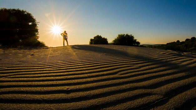 Foto homem em silhueta de pé na praia contra o sol brilhante no céu durante o pôr do sol