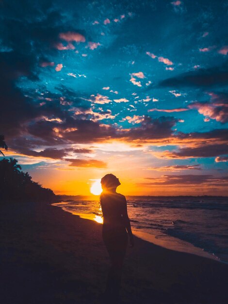 Foto homem em silhueta de pé na praia durante o pôr do sol