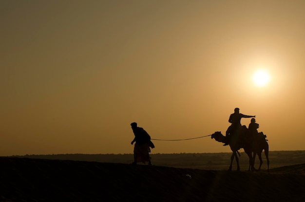 Foto homem em silhueta puxando camelos no deserto contra o céu durante o pôr do sol
