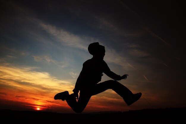 Foto homem em silhueta saltando contra o céu durante o pôr do sol