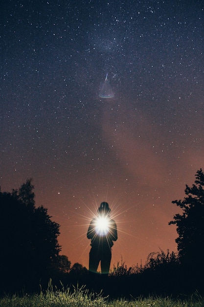 Foto homem em silhueta segurando uma lanterna no campo contra o céu à noite
