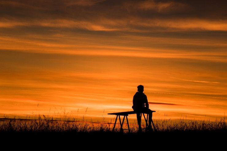 Foto homem em silhueta sentado no campo contra o céu durante o pôr do sol