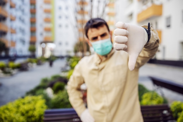 Homem em traje de proteção com máscara mostrando os polegares para baixo, caso de infecção de vírus, contaminação de germes ou bactérias. Prevenção de infecções e controle de epidemia. terno otetivo