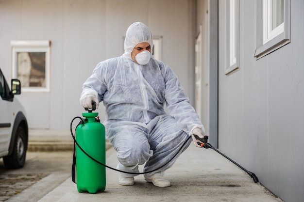 Homem em traje de proteção contra vírus e máscara de desinfecção de edifícios de coronavírus com o pulverizador. epidemia.