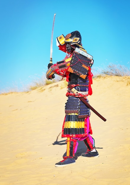 Homem em traje de samurai com espada correndo na areia. Homens com armadura de samurai correndo na areia. Personagem original