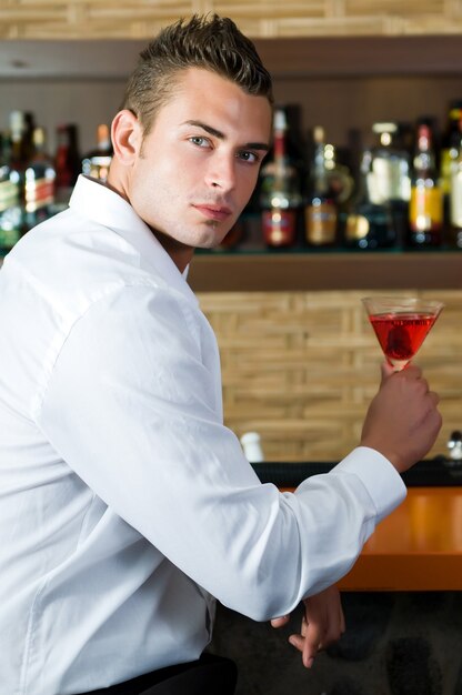 Homem em um bar com martini vermelho em um bar