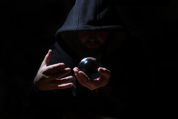 Foto homem em um capuz preto com bola de cristal invocar o mal