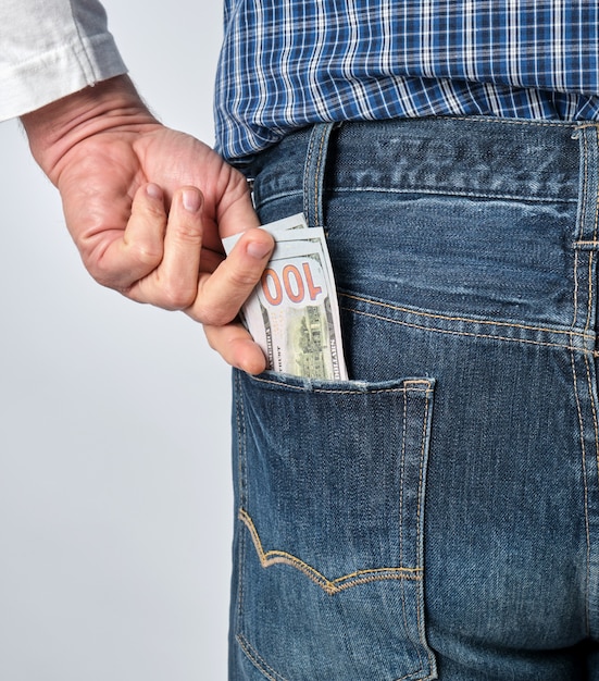 Homem em uma camisa xadrez azul e jeans coloca papel dólares americanos no bolso de trás