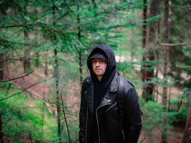 Ð homem em uma jaqueta de couro e um moletom com capuz em um fundo de floresta