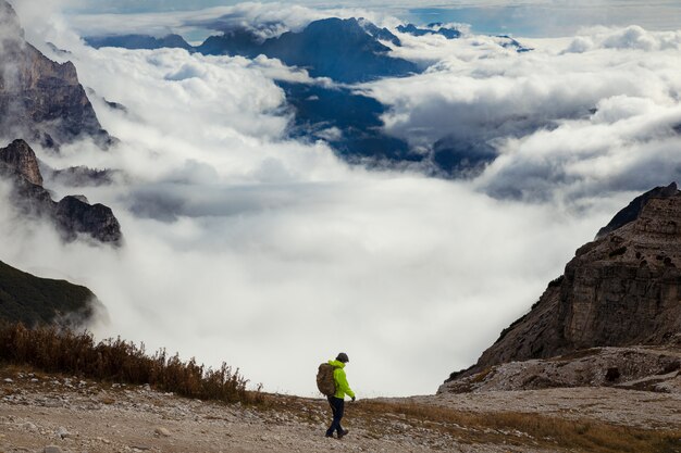 Foto homem em uma jaqueta verde com uma mochila, caminhadas nos alpes dolomitas cobertos de nuvens, vista incrível no parque tre cime di lavaredo, itália