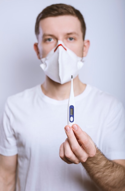 Homem em uma máscara médica detém um termômetro
