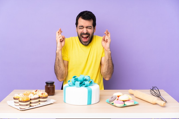 Homem em uma mesa com um bolo grande com dedos cruzando