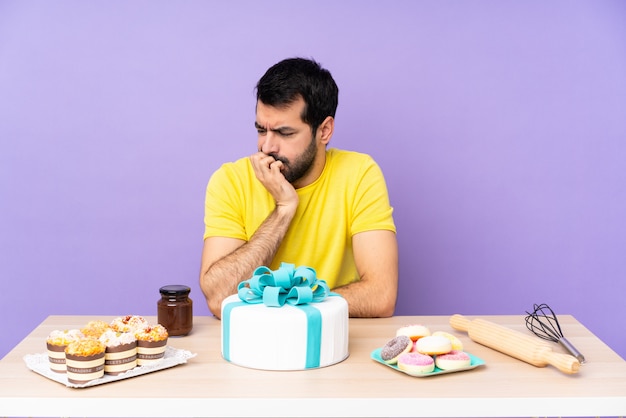 Homem em uma mesa com um bolo grande, com dúvidas