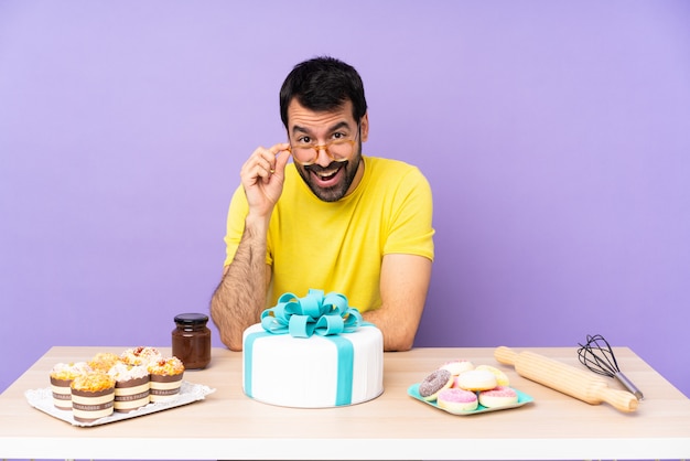 Homem em uma mesa com um bolo grande com óculos e surpreso