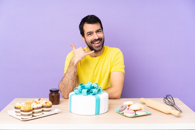 Homem em uma mesa com um bolo grande, fazendo gesto de telefone