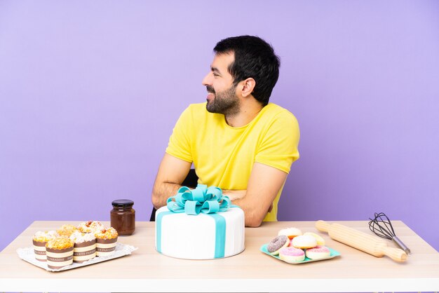 Homem em uma mesa com um bolo grande na posição lateral