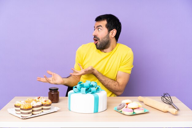 Homem em uma mesa com um grande bolo e expressão facial surpresa