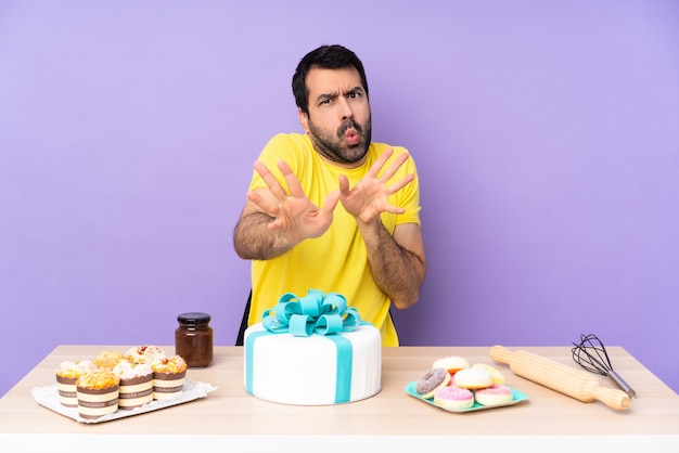 Homem em uma mesa com um grande bolo nervoso esticando as mãos para a frente
