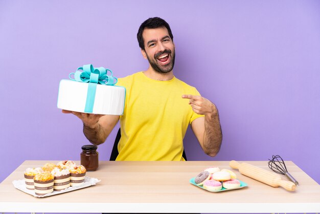 Foto homem em uma mesa com um grande bolo sobre parede roxa