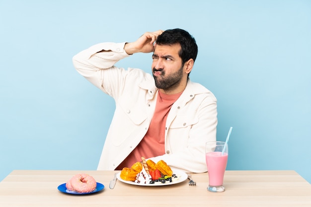 Homem em uma mesa com waffles sobre parede azul isolada