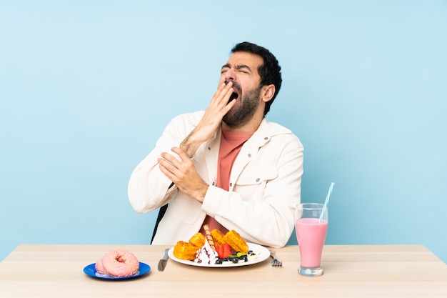 Homem em uma mesa com waffles sobre parede azul isolada