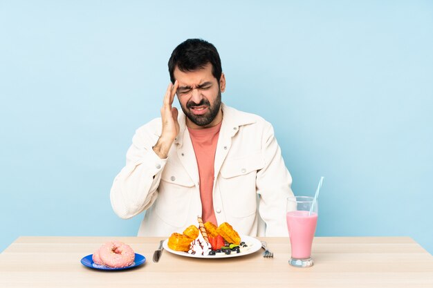 Homem em uma mesa tomando café da manhã waffles e um milk-shake com dor de cabeça