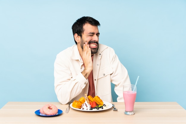 Homem em uma mesa tomando café da manhã waffles e um milk-shake com dor de dente