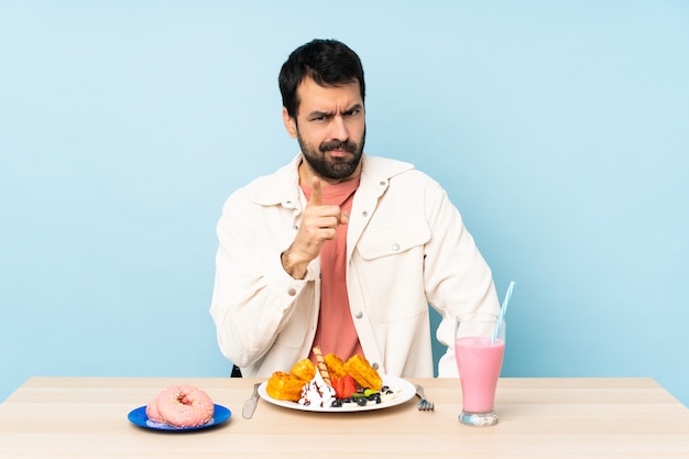 Homem em uma mesa tomando café da manhã waffles e um milk-shake frustrado e apontando para a frente