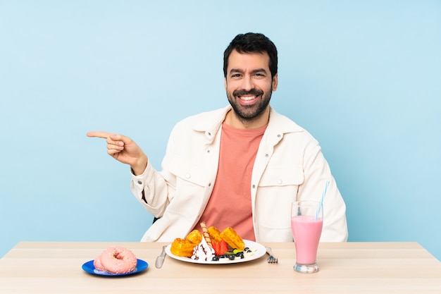 Homem em uma mesa tomando waffles de café da manhã e um milk-shake apontando o dedo para o lado