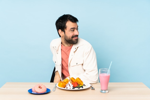 Homem em uma mesa tomando waffles de café da manhã e um milk-shake com os braços cruzados e feliz