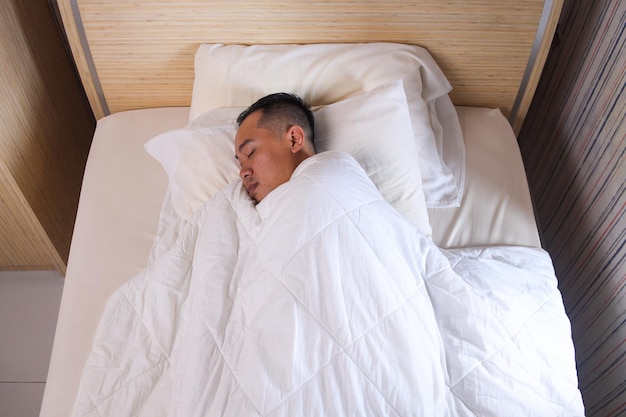 Homem embrulhado com cobertor macio branco dormindo na cama em casa