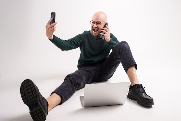 Homem emocional detém um telefone, tablet e laptop, se comunica e trabalha.