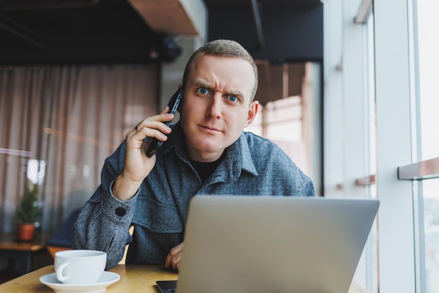 Homem emocional estudando web design durante e-learning à distância no laptop para pesquisa on-line conectando-se ao wifi no trabalho de netbook freelancing Conversa telefônica