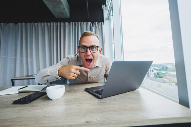 Homem emocional olhando para a câmera no local de trabalho um homem de óculos sentado em uma área de trabalho com um computador um estudante está procurando inspiração para novas idéias em um café de escritório