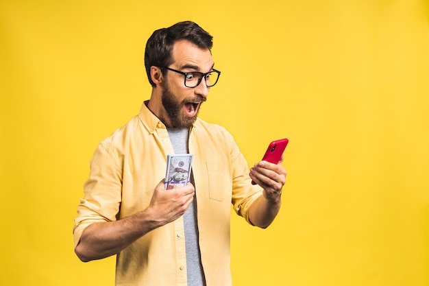 Homem empolgado casualmente segurando muito dinheiro em moedas de dólar e usando o telefone