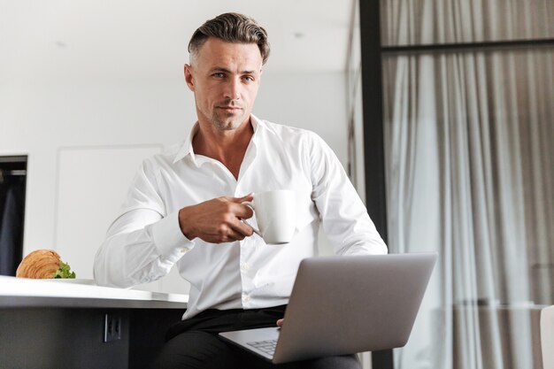 Homem encantador vestido com roupas formais usando laptop