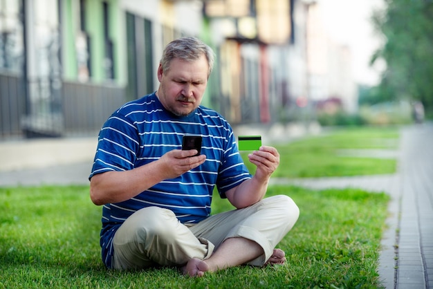 Homem encontra ofertas de comércio eletrônico para comprar online com telefone e cartão de crédito no gramado da cidade