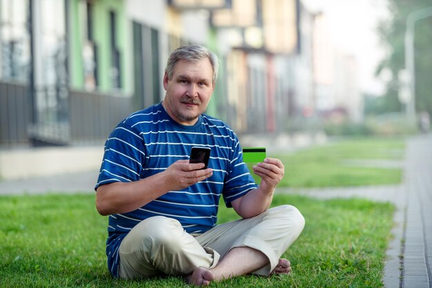 Homem encontra ofertas de comércio eletrônico para comprar online com telefone e cartão de crédito no gramado da cidade