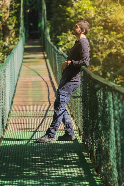 Homem encostado no corrimão de uma ponte suspensa