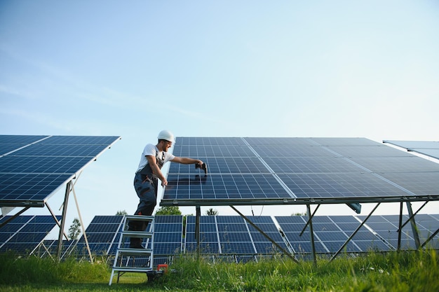 Homem engenheiro de uniforme trabalhando na fazenda de energia de painéis solares Campo de painéis solares Produção de energia limpa Energia verde