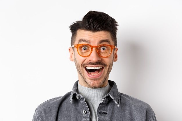 Homem engraçado animado de óculos sorrindo, olha com espanto e alegria na incrível promoção, feliz em pé contra um fundo branco.