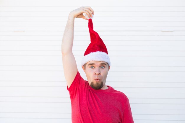 Homem engraçado bonito com chapéu de Papai Noel se divertir na parede branca