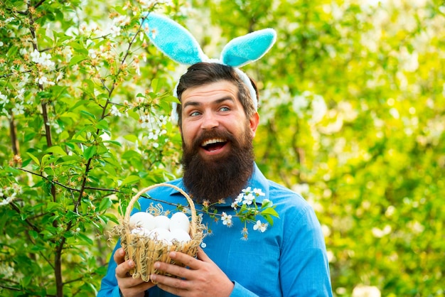 Homem engraçado com fantasia de coelho segura ovos de páscoa Homem barbudo segurando cesta de ovos de páscoa