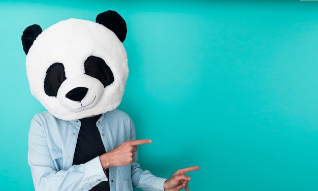 Homem engraçado com máscara de panda apontando os dedos para o lado sobre a parede azul-água-marinha