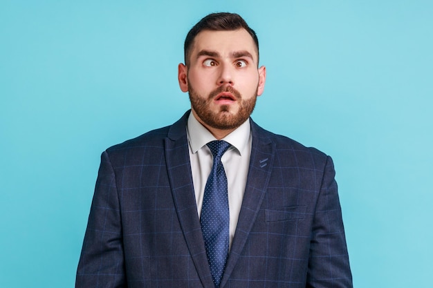 Homem engraçado divertido com barba vestindo terno estilo oficial cruzando os olhos parecendo louco e estúpido, brincando, se divertindo, problemas de visão. Tiro de estúdio interior isolado sobre fundo azul.