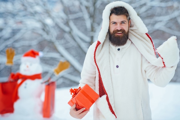 Homem engraçado do Papai Noel posando com caixa de presente vermelha no inverno