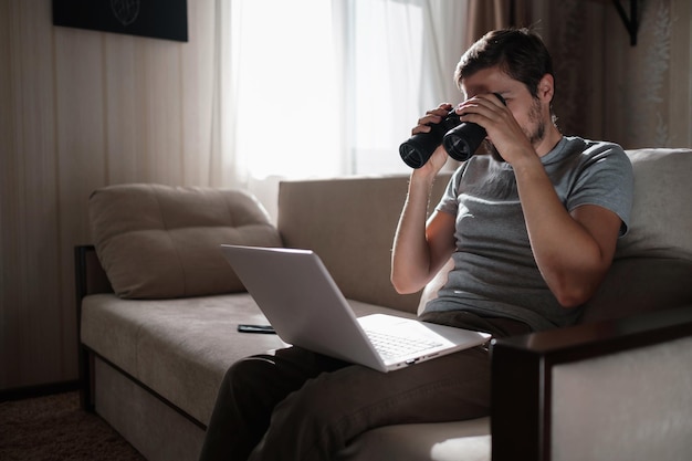 Homem engraçado procurando binóculos procurando um laptop na mesa trabalhando em home office