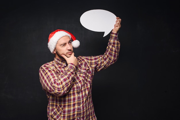 Homem engraçado sério no chapéu de Papai Noel de Natal vermelho contém papelão branco vazio como em branco ou simulado com espaço de cópia para o texto. Fundo preto