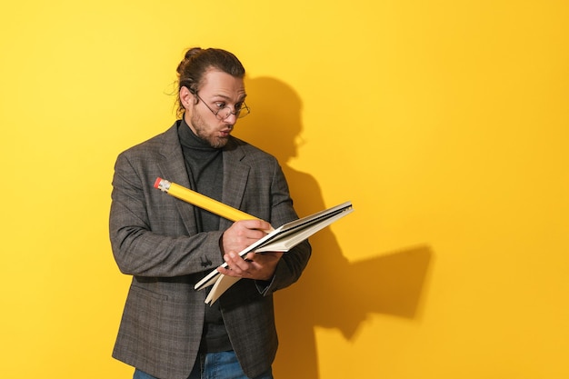 Homem engraçado usando óculos segurando lápis grande e caderno em fundo amarelo