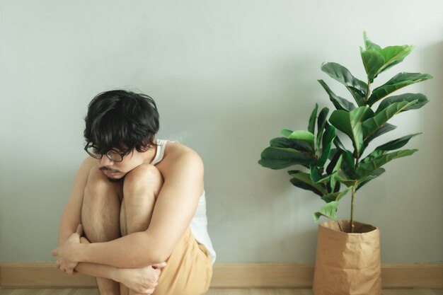 Homem entediado solitário senta-se desesperadamente no chão com a planta da casa na sala.